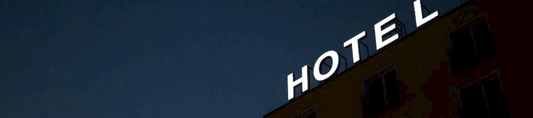 The image shows a building with the word "HOTEL" on top against a dark sky, with lights illuminating the letters.