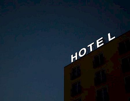 The image shows a building with the word "HOTEL" on top against a dark sky, with lights illuminating the letters.