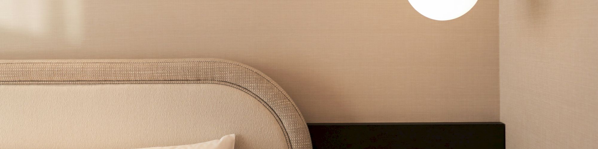 The image shows a minimalist bedroom with a headboard, pillow, and a modern pendant light hanging beside the bed on a plain wall.