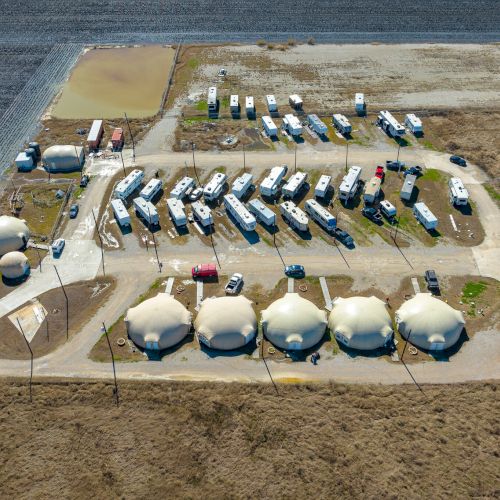 The image shows an aerial view of a campsite with several RVs, dome tents, and parked vehicles arranged in a designated area.