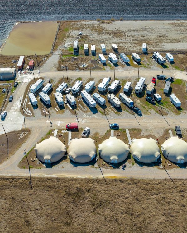 The image shows an aerial view of a campsite with several RVs, dome tents, and parked vehicles arranged in a designated area.