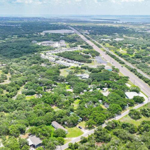 An aerial view of a vast green landscape divided by a highway, with scattered houses and buildings throughout the area.