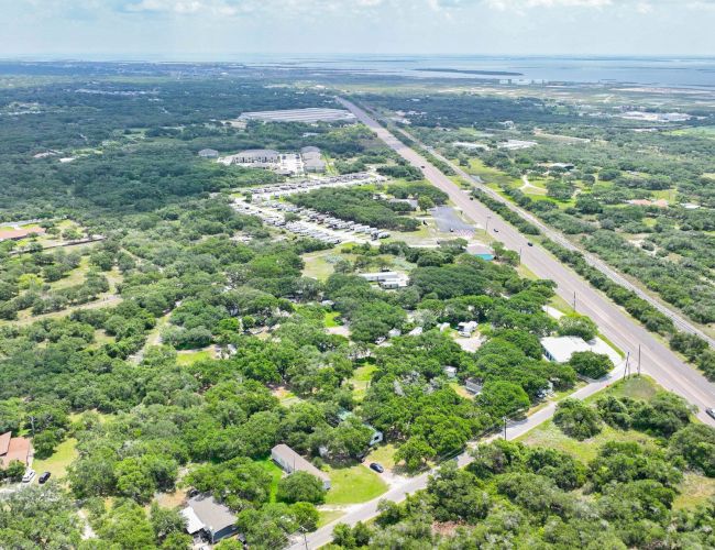 An aerial view of a vast green landscape divided by a highway, with scattered houses and buildings throughout the area.