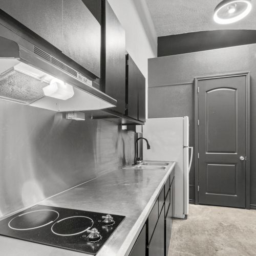 A modern kitchen with a stovetop, metallic counters, range hood, sink, refrigerator, and cabinets in monochrome colors.
