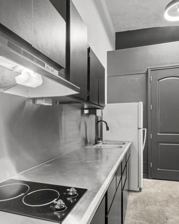A modern kitchen with a stovetop, metallic counters, range hood, sink, refrigerator, and cabinets in monochrome colors.