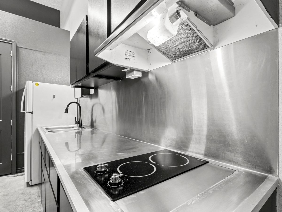A modern kitchen with a stove, stainless steel countertops, a sink, and a refrigerator in black and white tones completes the scene.