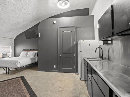 A small, modern studio apartment with a bed, refrigerator, sink, and cabinets in a minimalist design.